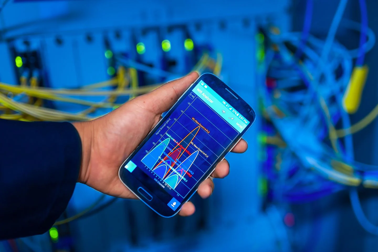 Celular exibindo dados de análise de rede diante de equipamentos de servidor